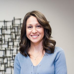 A woman standing in front of a wall with a smile.