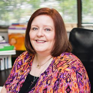 A woman sitting in an office chair wearing a colorful jacket.