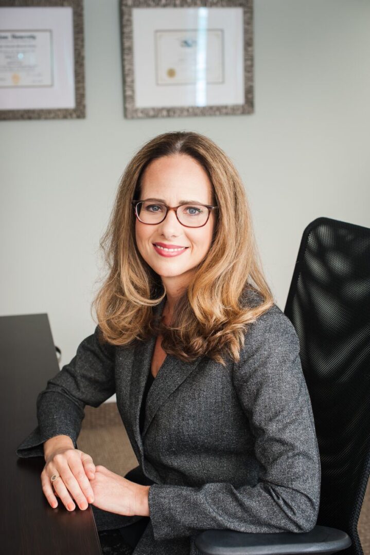 A woman sitting at her desk in front of a black chair.