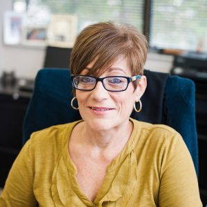 A woman sitting in an office chair wearing glasses.
